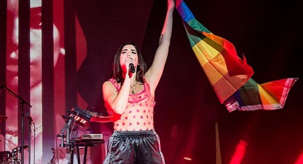 Dua Lipa on stage holding up a rainbow flag