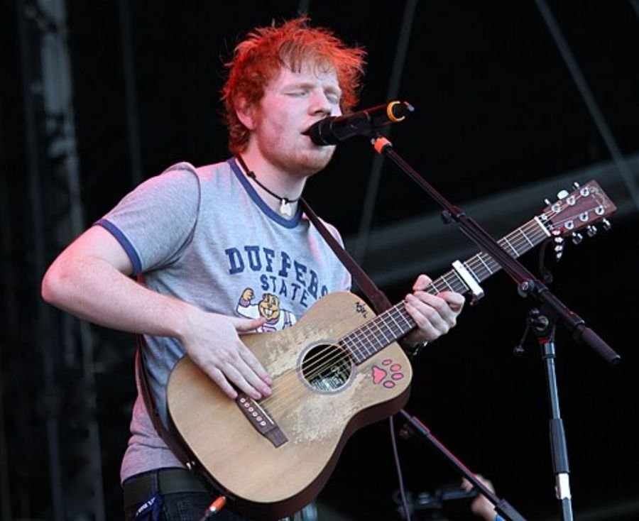 Musician in a grey t-shirt singing and playing an acoustic guitar on stage, shown in the independent years section
