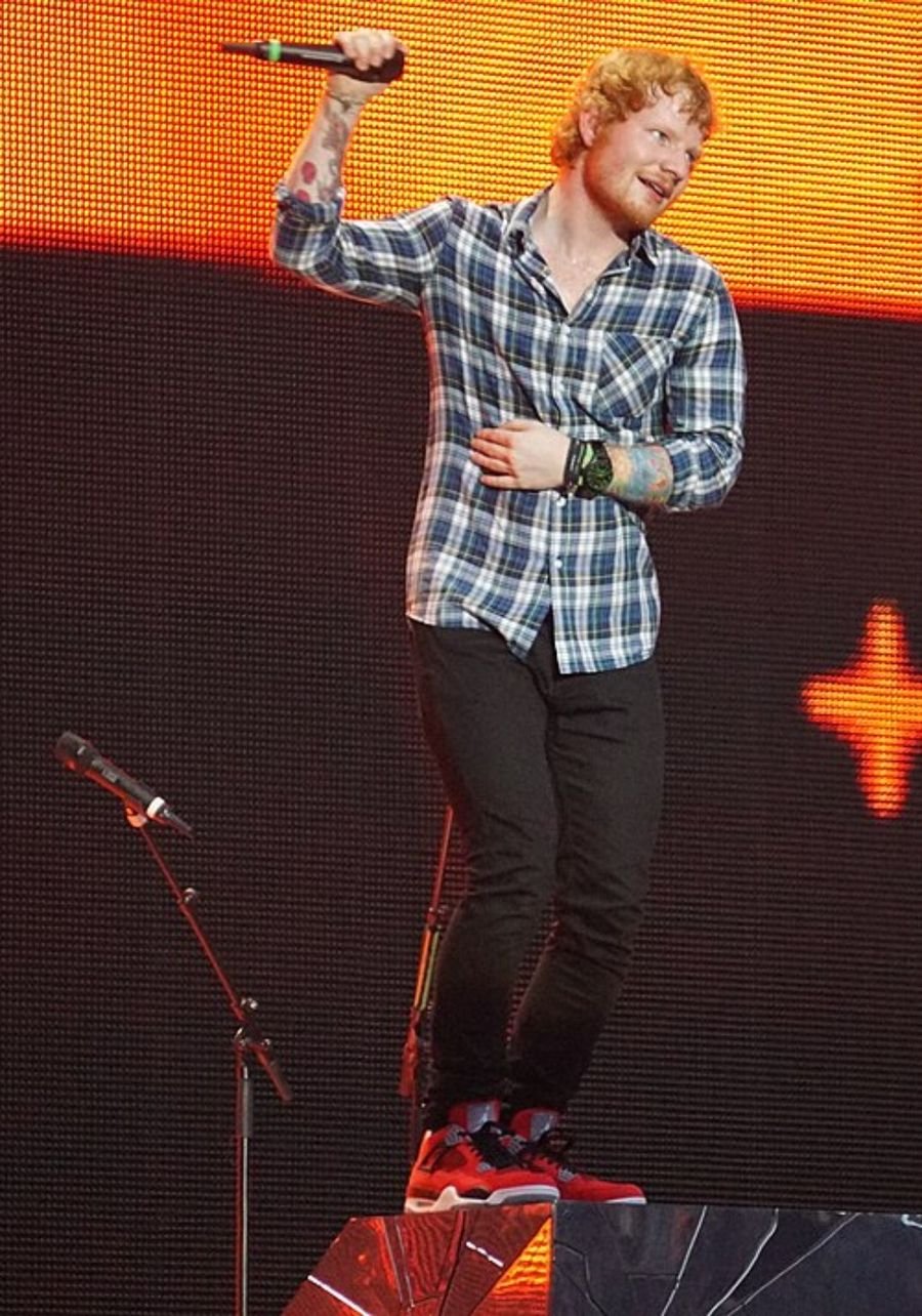 Musician in a checked shirt holding a microphone on a stage with orange lights, shown in the breakthrough section