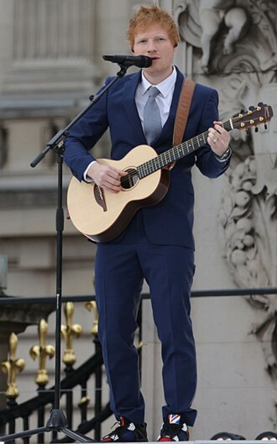 Musician in a navy suit playing an acoustic guitar at a microphone outdoors, shown in the Divide album section