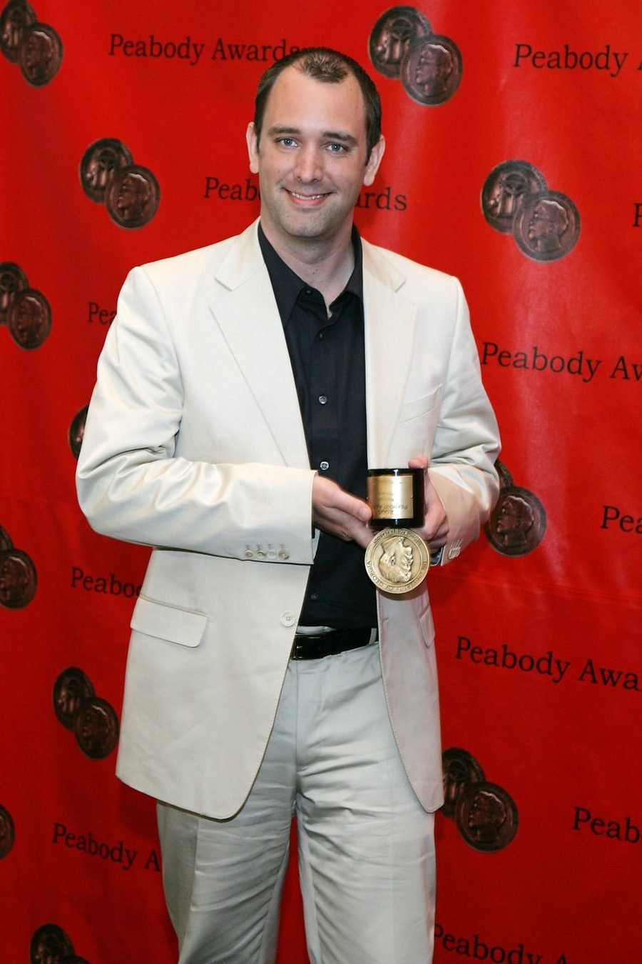 Man in a light suit holding a medal in front of a Peabody Awards backdrop, shown in the awards section